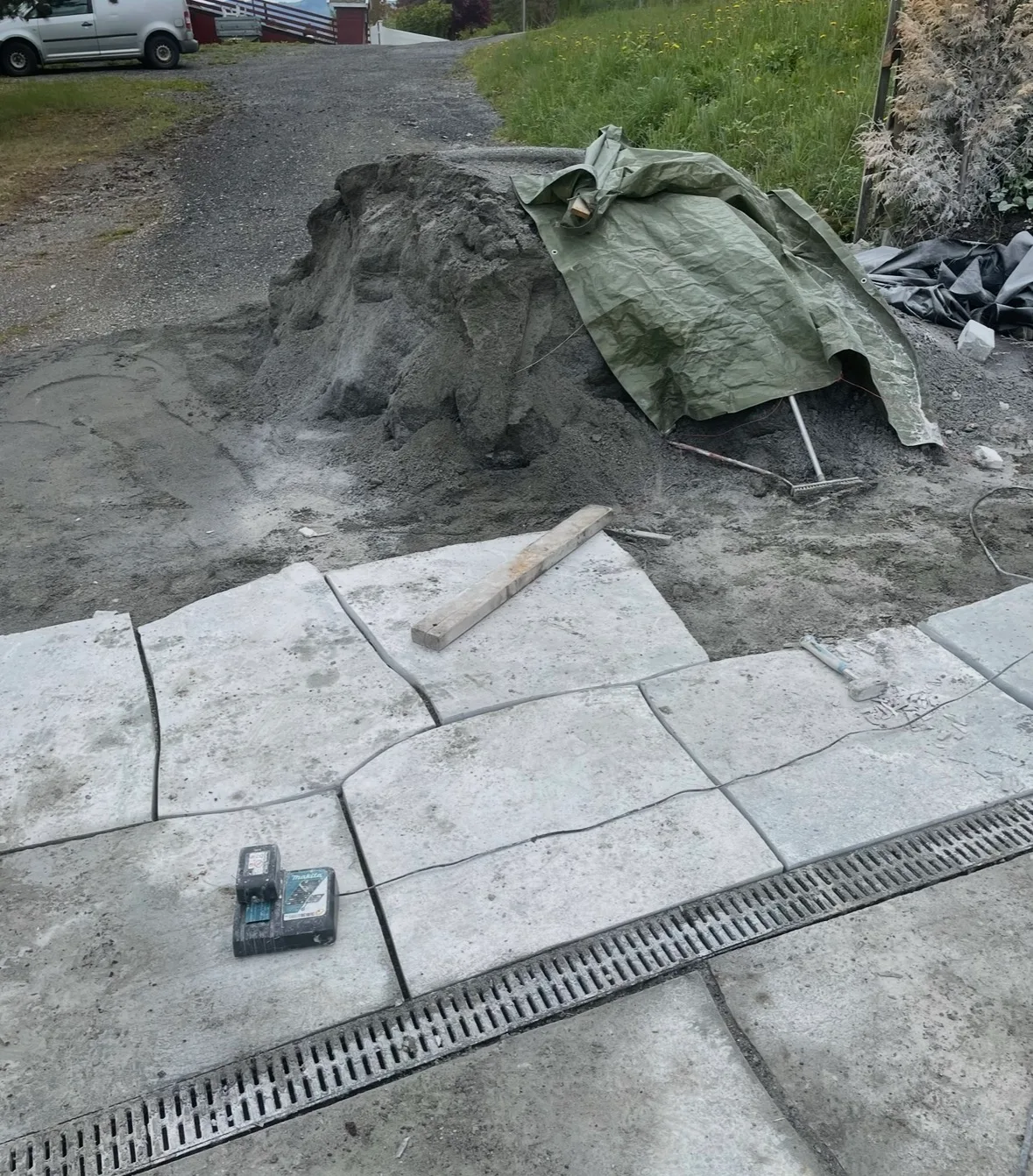 Grå belegningsstein som legges på en byggeplass med sand og verktøy